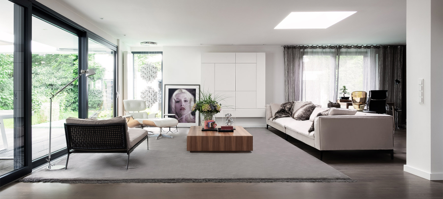 A living room of a private residence in Munich with a big white sofa, a brown center table, a white reclaimed chair, a lamp and a paint on the wall.  kitzig design studios Kitzig Design Studios- From Germany to the World Interior INTERNET Wohnraeume Bungalow Muensterland 02 1
