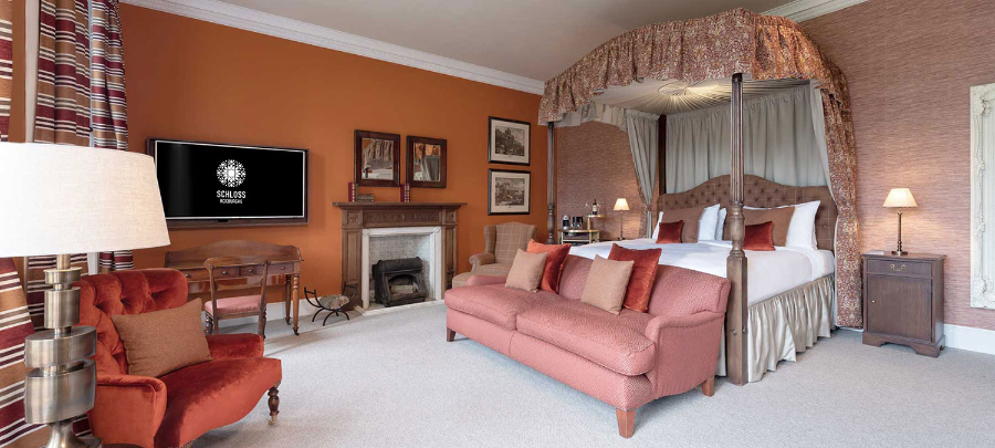 A bedroom in SCHLOSS Roxburghe, decorated in shades of pink and orange. The room has a big bed, a pink sofa and a orange/red armchair. kitzig design studios Kitzig Design Studios- From Germany to the World Schloss Roxburghe SZ 01 2
