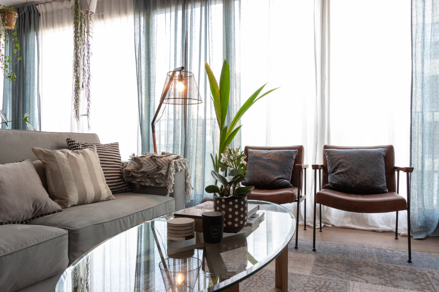 Ivy's Design - The twist we didn't know we needed EDITA’S APARTMENT. In the picture we have two brown armchairs with pillows on top, a beige sofa, some blue curtains and a glass table with some plants in the center.  ivy's design Ivy’s Design – The twist we didn’t know we needed The Twist of Ivys Design in Modern Interior Decor Editas Apartment decor
