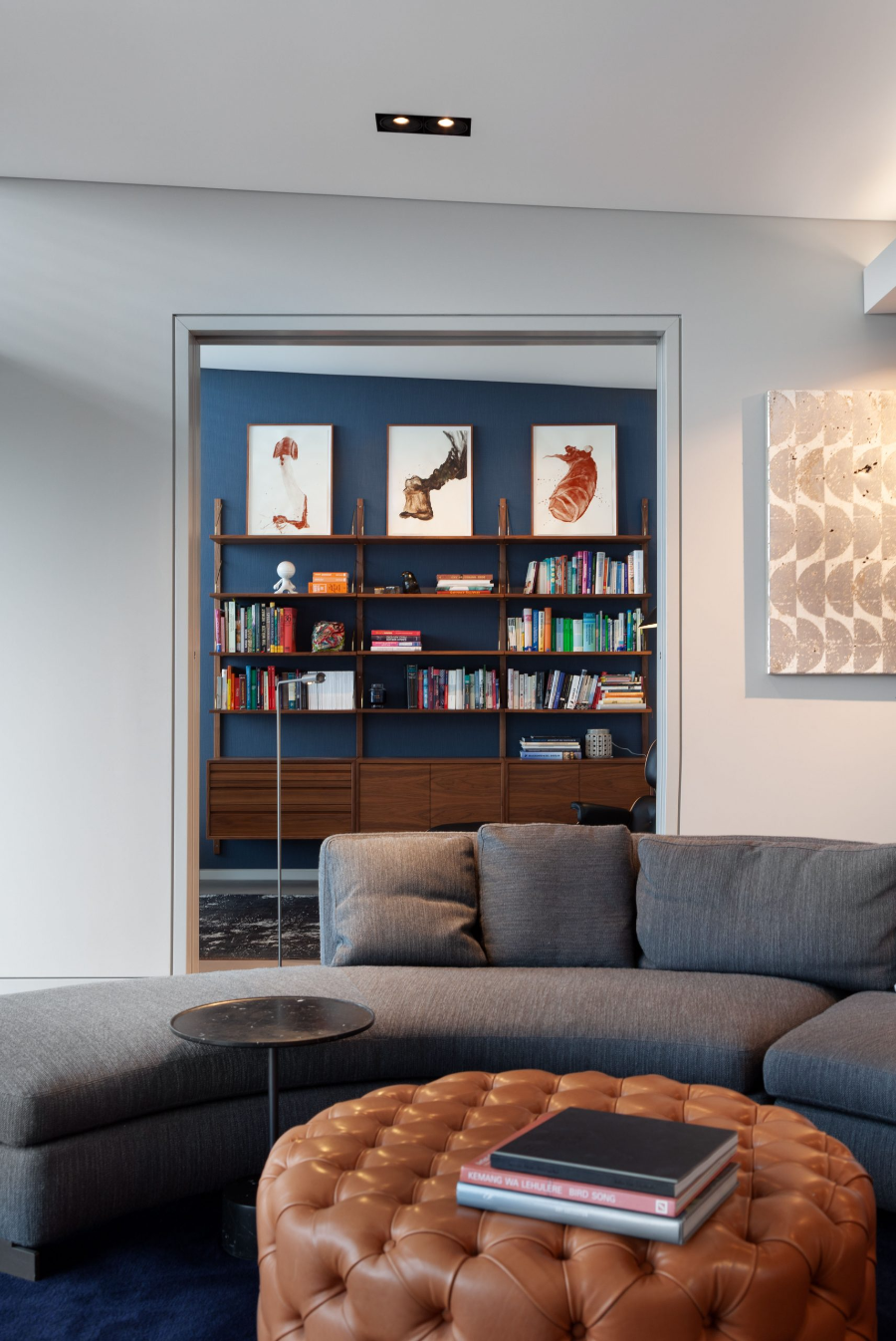 Dopo Domani, LOFT IN DER STADT living room with a grey sofa, a dark wood bookcase against a blue wall. dopo domani 10 Stunning Dopo Domani Interiors To Inspire You 20200110 dopo domani loft B 013 scaled 1