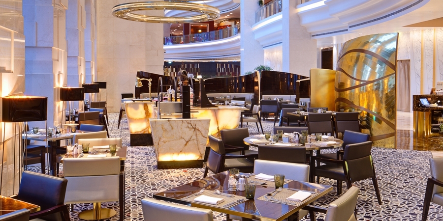 An open dining room with marble center tables, gold details, bespoke wood dining tables and white and black leather armchairs. hba HBA – The Best Interior Design Projects in Dubai HBA2