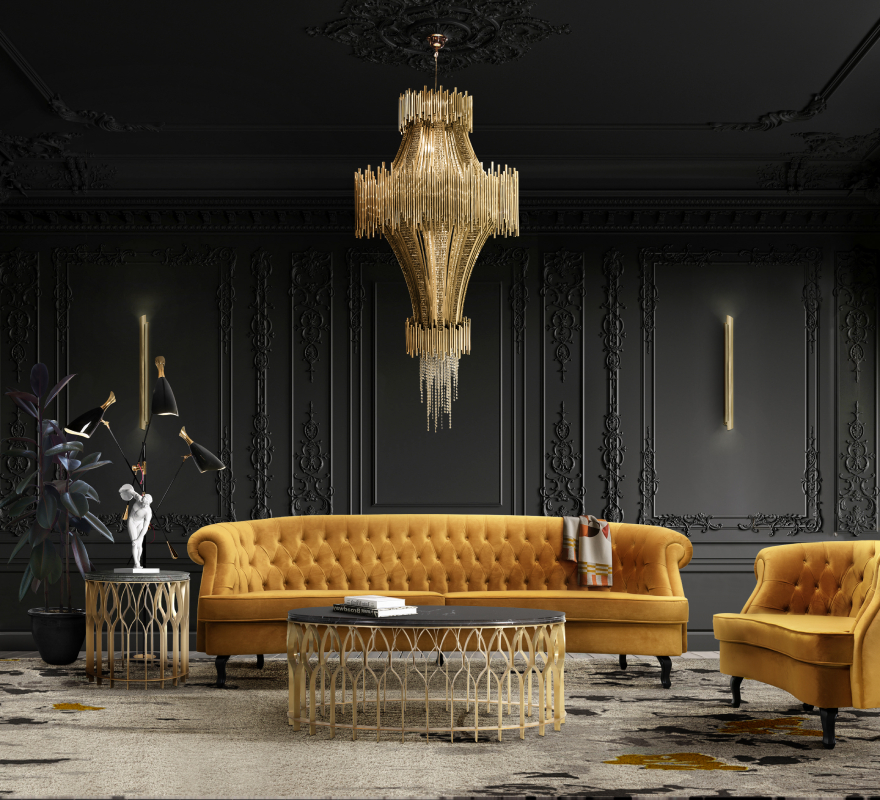 Dramatic high-end living room with ornate black wall molding, vibrant mustard-yellow velvet tufted seating, a monumental gold tiered chandelier, and a black marble coffee table on an abstract patterned rug.